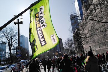 Eine BUND Fahne Richtung wolkenlosen Himmel wird hochgehalten, im unteren Teil des Bildes sieht man die Demonstranten auf der Straße