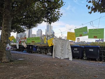 Schnur mit Zetteln und Botschaften zwischen Bäumen vor Frankfurter Skyline zum World Cleanup Day