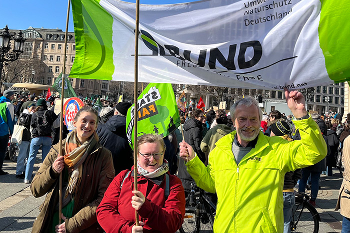 Die Bundesfreiwilligendienstleistenden halten zusammen mit dem Vorsitzenden des OV Nord das Banner des BUND hoch auf dem Vorplatz der Alten Oper Frankfurt, wo sich viele Menschen im Hintergrund versammelt haben
