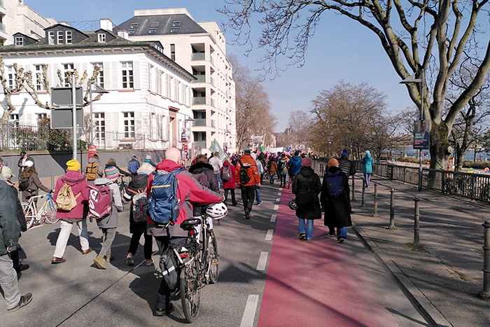 Mehrere Menschen, zu Fuß und mit Fahrrad demonstrierend entlang des Mainufers.