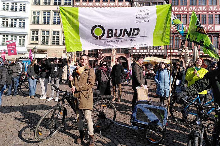 Bundesfreiwilligendienstleistende hält auf Frankfurter Römerplatz BUND Banner hoch und hält Fahrrad fest